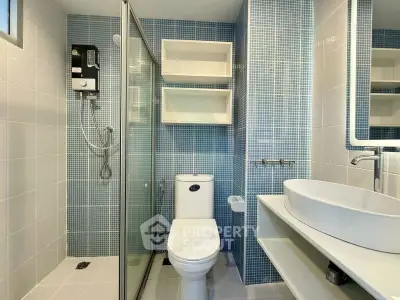 Modern bathroom with glass shower, sleek fixtures, and blue mosaic tiles.
