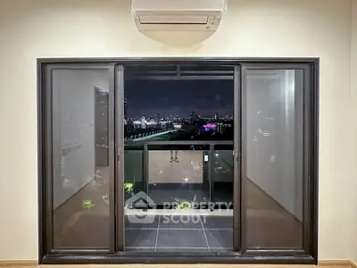 Modern apartment with balcony offering stunning night city view, featuring sleek sliding glass doors and air conditioning.