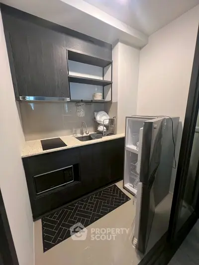 Compact modern kitchen with sleek black cabinetry and stainless steel appliances.