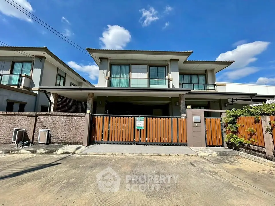 Modern two-story house with spacious driveway and wooden gate under clear blue sky.