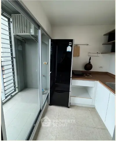 Modern kitchen with sleek black fridge and open layout, adjacent to a balcony with sliding glass doors.