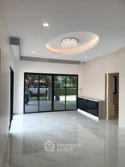 Spacious modern living room with elegant chandelier and large windows offering natural light.