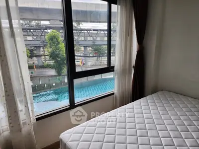 Bright bedroom with large window overlooking pool and urban view, perfect for modern living.
