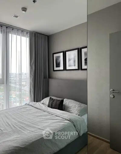 Modern bedroom with large window and city view, featuring stylish decor and cozy bedding.