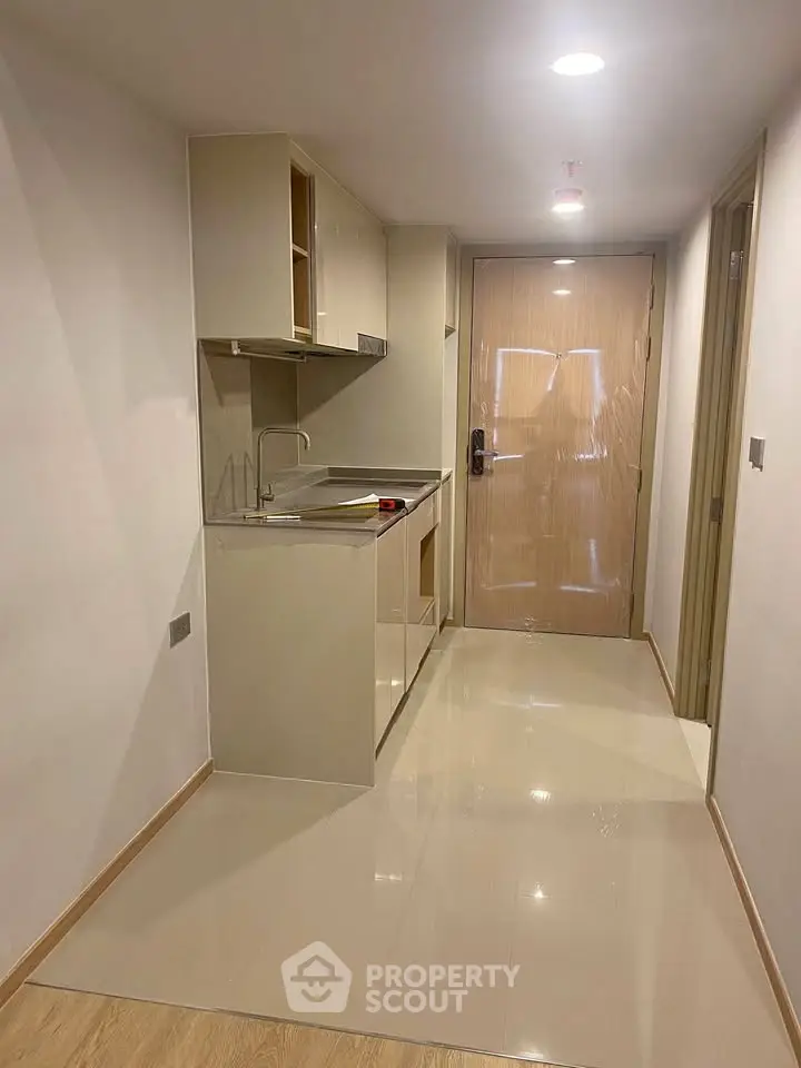 Modern compact kitchen in a sleek apartment hallway with glossy floor tiles.