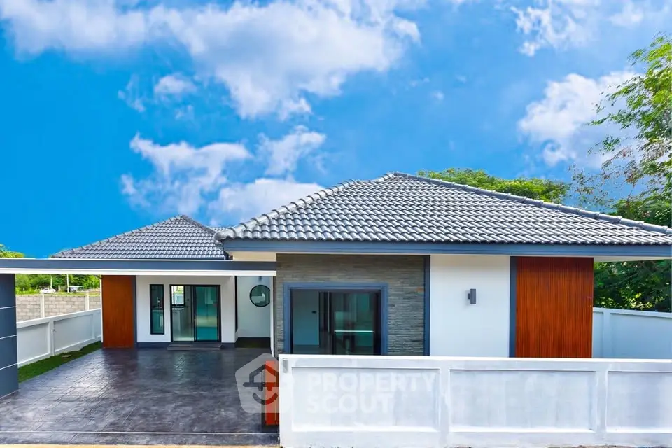 Modern single-story house with sleek design and spacious driveway under a bright blue sky.