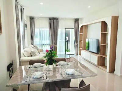 Elegant living room with modern decor and dining area, featuring large windows and stylish furniture.