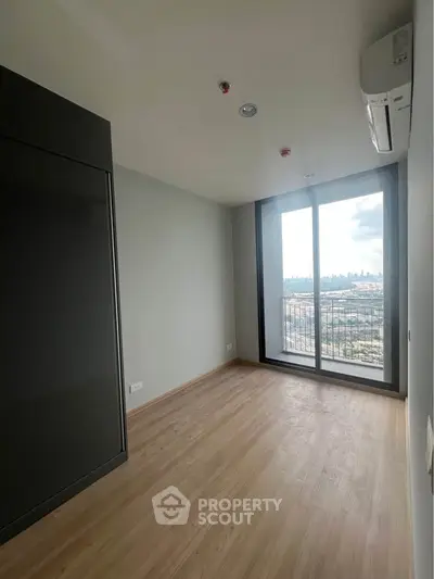 Spacious room with large window offering stunning city view and sleek wooden flooring.