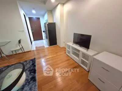Modern living room with wooden flooring, compact TV setup, and open kitchen layout.