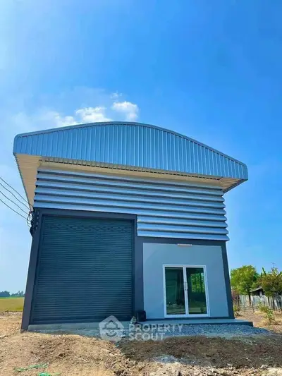 Modern industrial building with sleek metal facade and large roller door under clear blue sky.