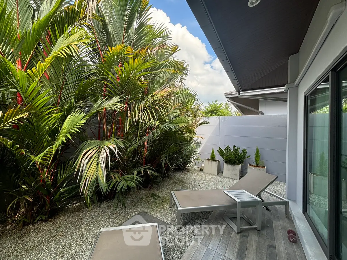 Charming garden patio with lush greenery and modern lounge chairs, perfect for relaxation.