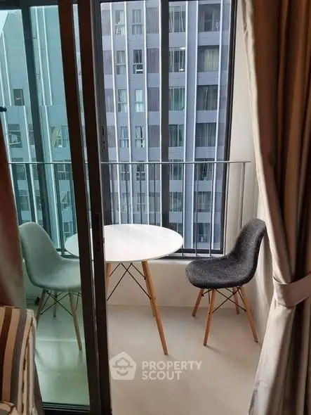 Chic urban balcony with modern chairs and table, offering a cityscape view through glass doors.
