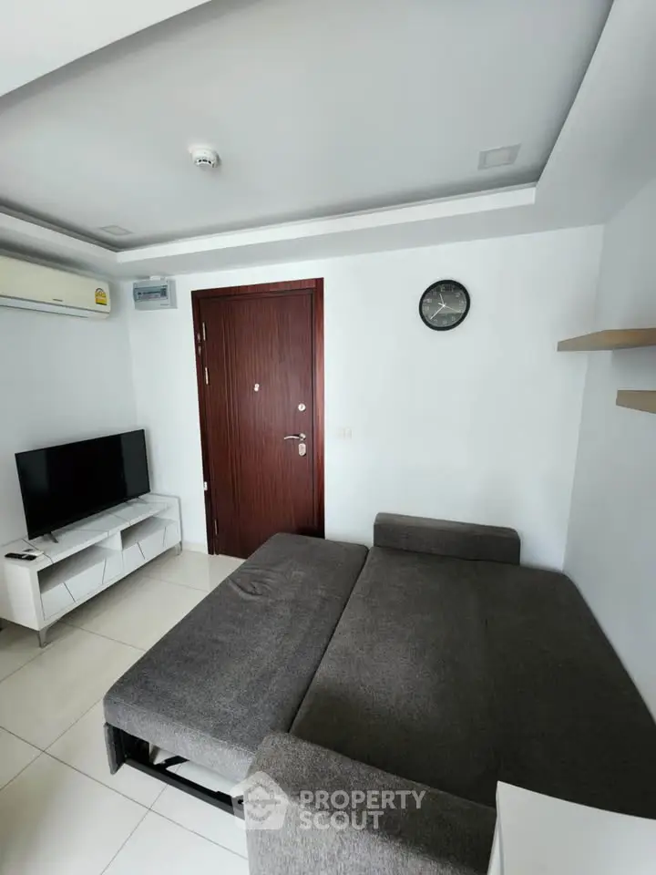 Modern living room with sleek gray sofa and wall-mounted TV in a minimalist apartment.