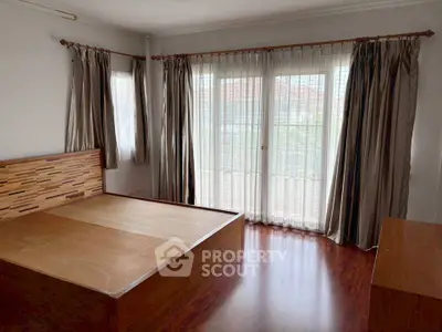 Spacious bedroom with wooden flooring and large windows for natural light.