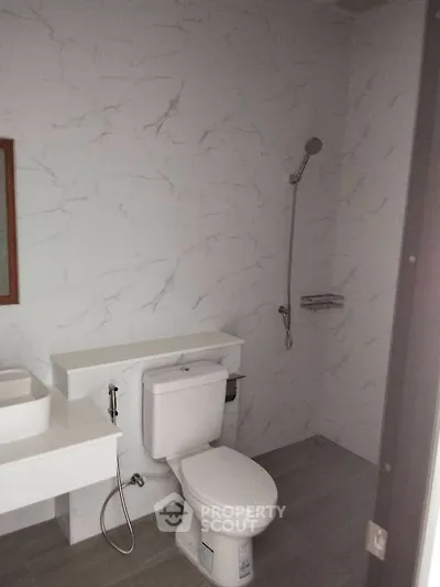Modern bathroom with sleek design and marble walls, featuring a toilet and shower area.