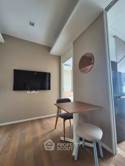 Modern living space with wall-mounted TV and compact dining area, featuring sleek wooden flooring.