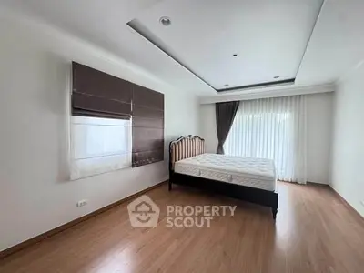 Spacious bedroom with wooden flooring and large windows for natural light.