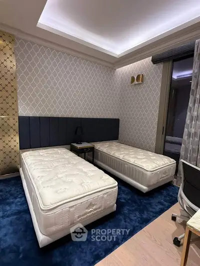Modern bedroom with twin beds, stylish wallpaper, and plush blue carpet in a contemporary apartment.