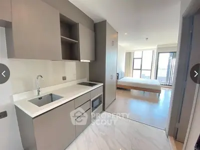 Modern open-plan kitchen with sleek cabinetry and built-in appliances seamlessly transitions to a cozy bedroom with ample natural light and a welcoming ambiance.