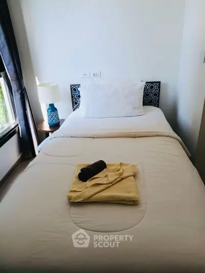 Cozy bedroom with single bed, stylish lamp, and natural light from window.