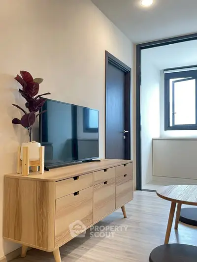 Modern living room with sleek wooden furniture and flat-screen TV, bright natural light.