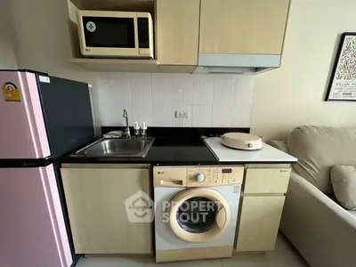 Compact kitchen with washing machine, microwave, and fridge in modern apartment.