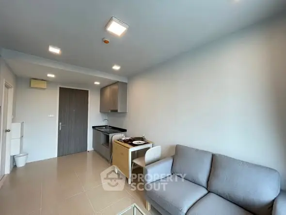 Modern living room with compact kitchen and cozy sofa in open layout apartment.