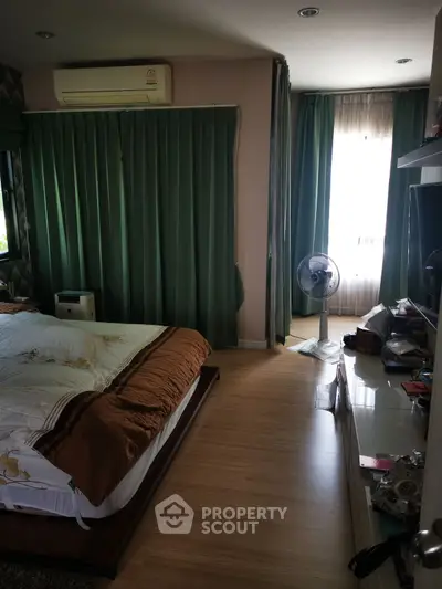 Cozy bedroom with wooden flooring and green curtains, featuring a comfortable bed and air conditioning.