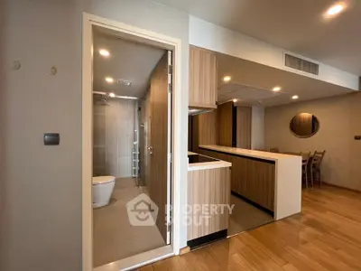 Modern open-layout kitchen with wooden cabinetry and adjacent bathroom in a stylish apartment.