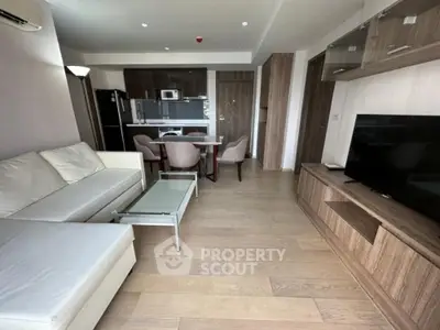 Modern living room with open kitchen, featuring sleek furniture and wooden flooring.