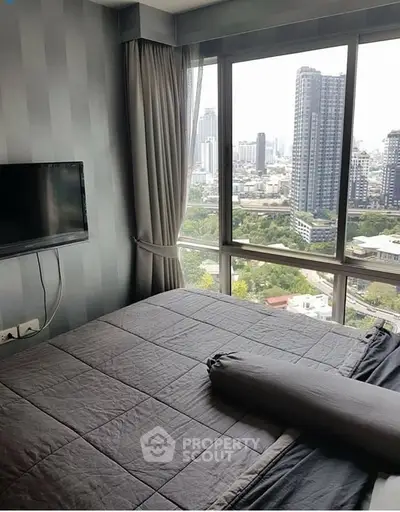 Modern bedroom with city view and wall-mounted TV in high-rise apartment.