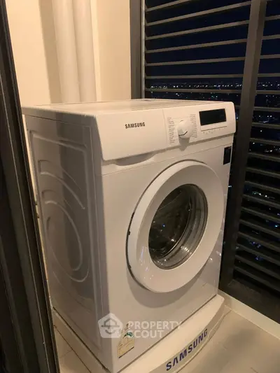 Modern washing machine in a high-rise apartment with city night view.