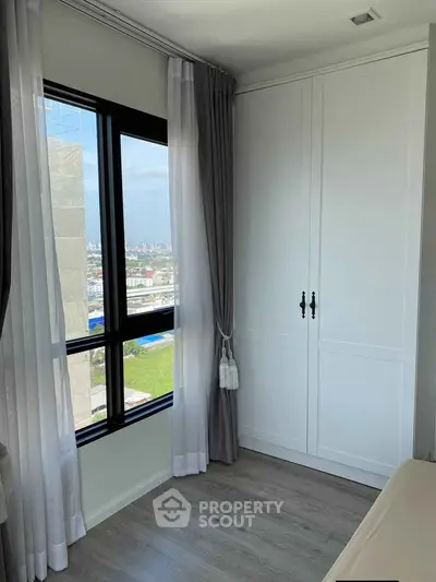 Bright bedroom with large window and white wardrobe offering city views.