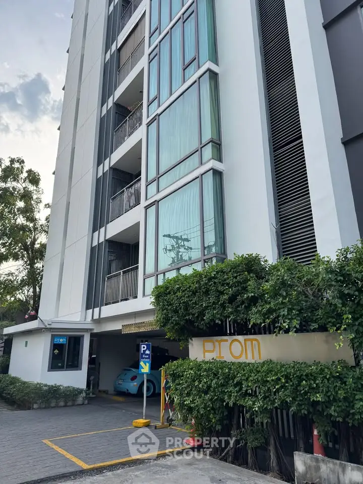Modern apartment building exterior with parking area and lush greenery.