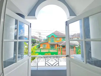 Charming balcony view with open doors overlooking colorful neighborhood houses.