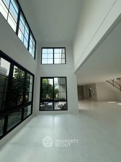 Spacious modern living room with high ceilings and large windows offering natural light and garden view.