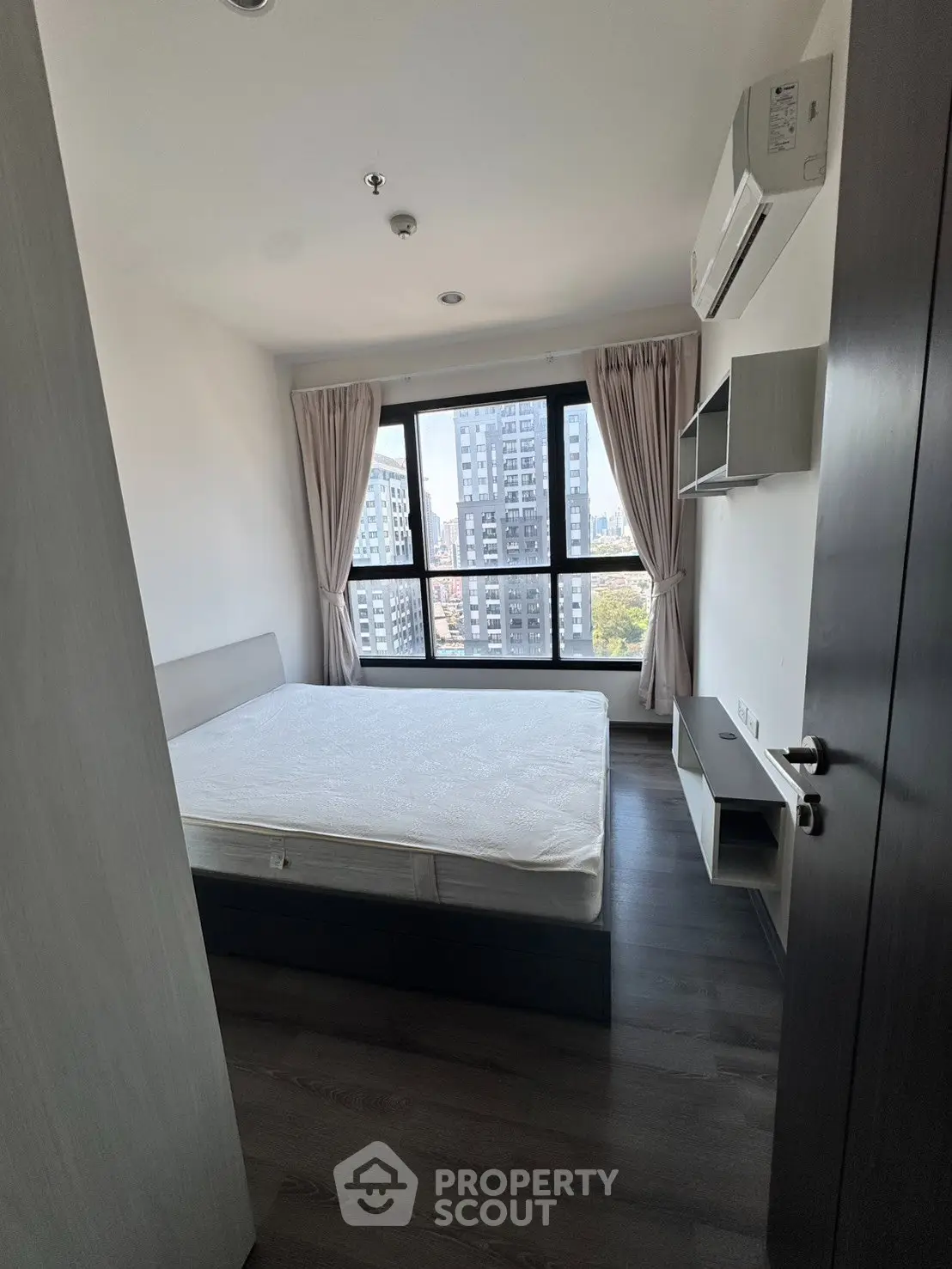 Modern bedroom with large window offering city view, featuring a comfortable bed and air conditioning.