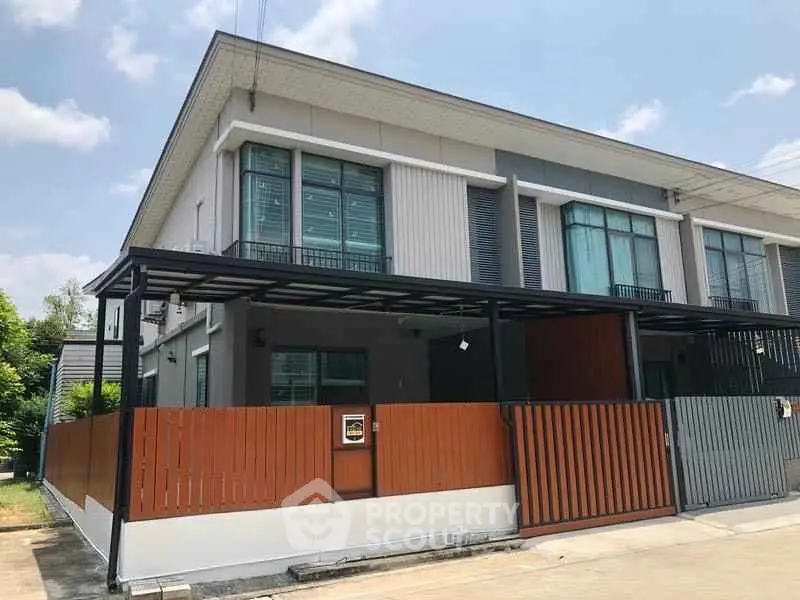 Modern two-story townhouse with sleek design and gated entrance in a sunny neighborhood.