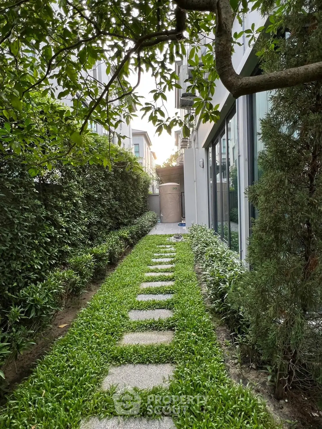 Charming garden pathway with lush greenery and modern building exterior, perfect for serene outdoor living.