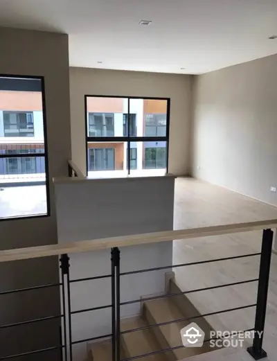 Spacious and modern living room with abundant natural light, featuring large windows and a sleek staircase leading to an elevated area.