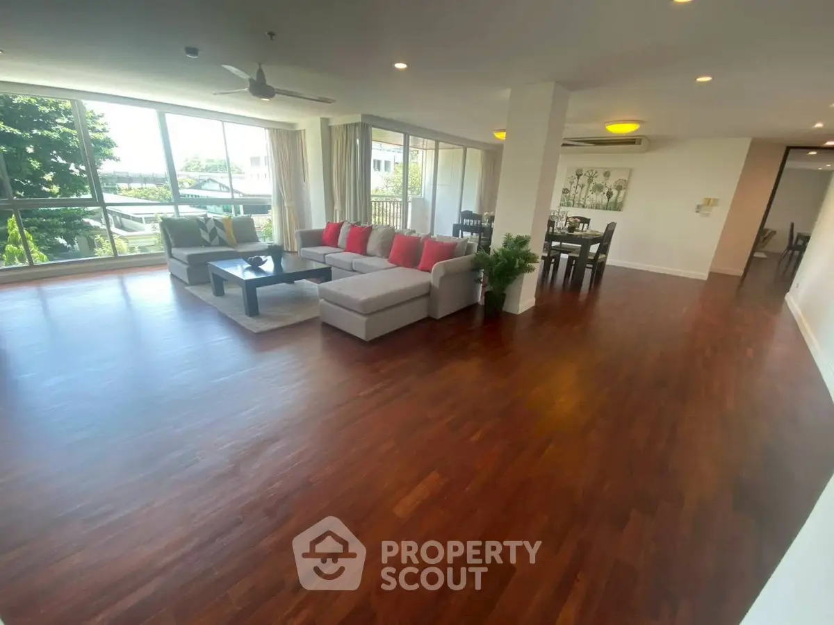 Spacious living room with hardwood floors and large windows offering natural light and garden views.