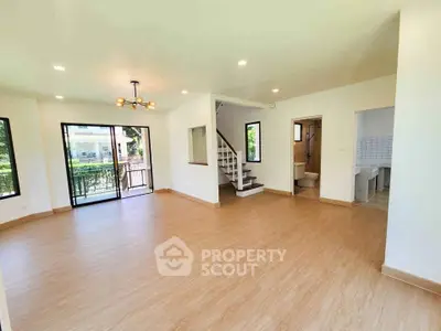 Spacious open-plan living room with modern lighting and wooden flooring, featuring large windows and balcony access.