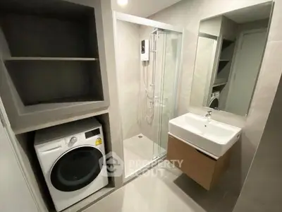 Modern bathroom with shower and washing machine in sleek apartment.