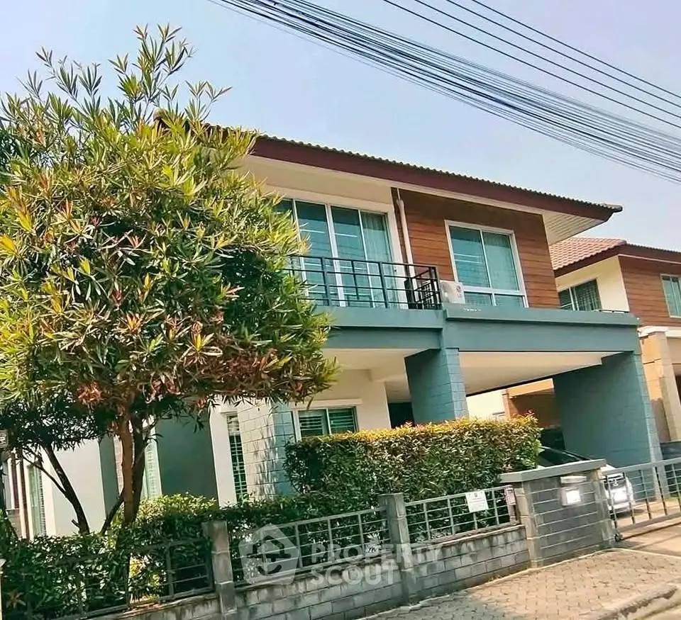 Modern two-story house with balcony and lush greenery in a suburban neighborhood.