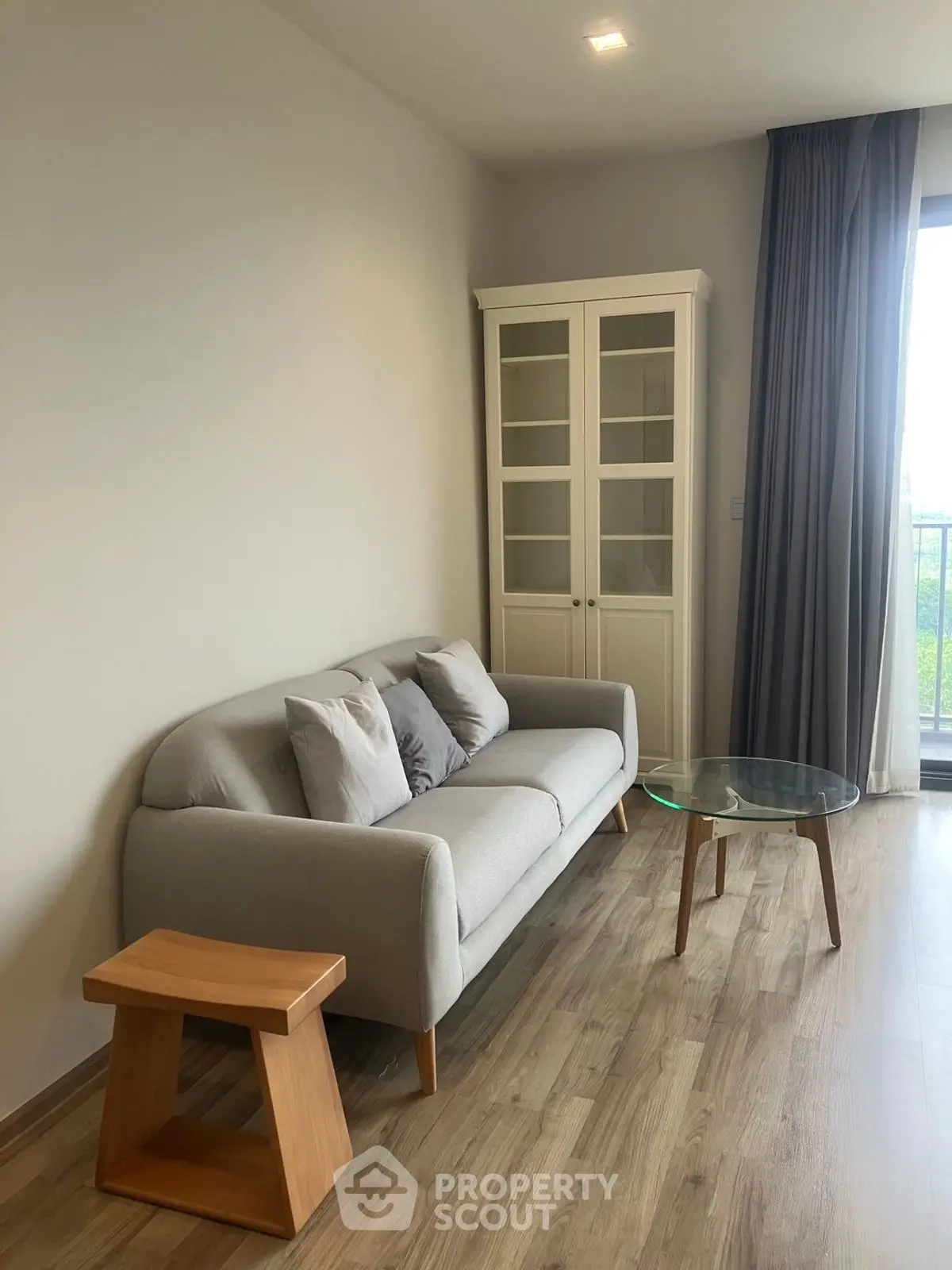 Modern living room with cozy sofa, glass coffee table, and elegant cabinet near balcony.