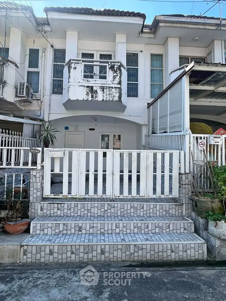 Charming two-story townhouse with a balcony and gated entrance, ideal for urban living.