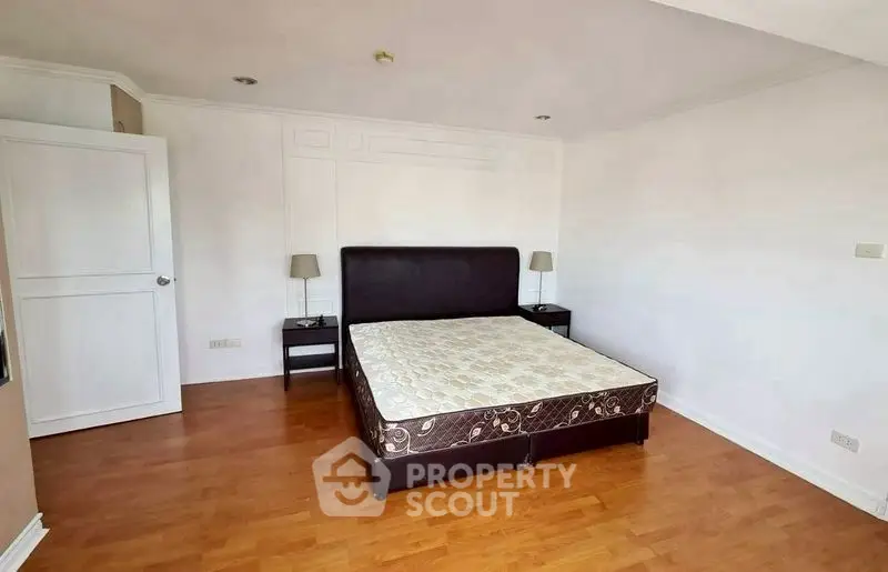 Spacious bedroom with wooden flooring and elegant bed frame in modern apartment.