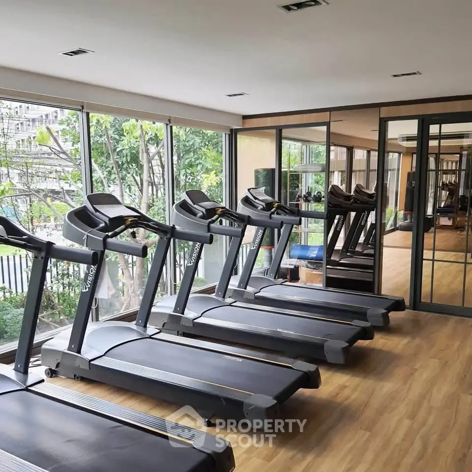 Modern gym with multiple treadmills and large windows overlooking greenery.