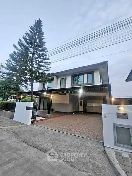 Modern two-story house with spacious driveway and tall pine tree in front yard.