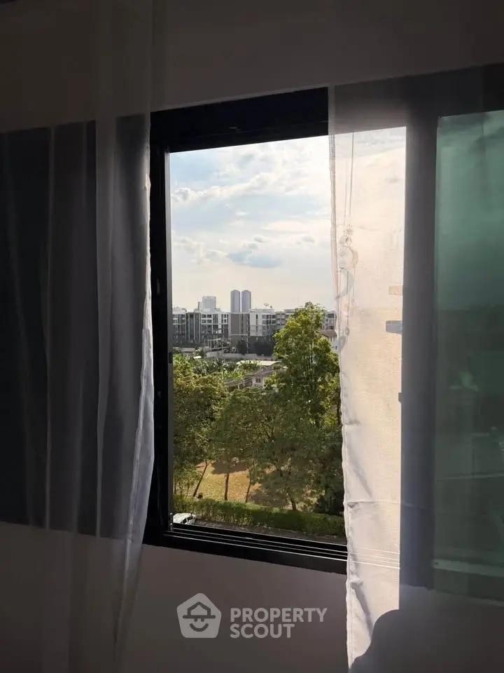 Scenic view from a window overlooking a lush green park and modern buildings.